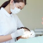 歯のクリーニング中に手を上げて痛みを訴える女性