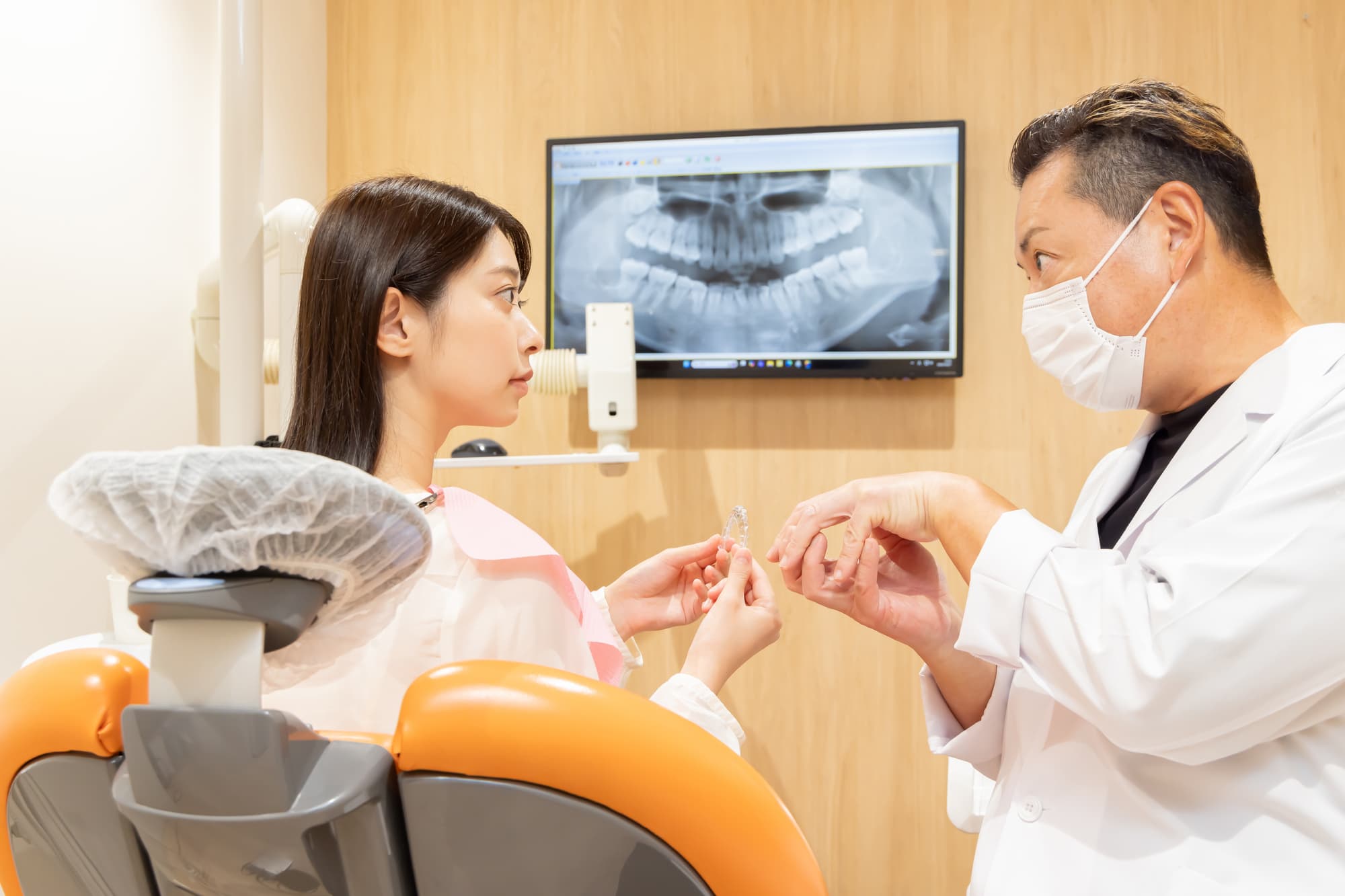 インビザライン矯正中に痛みが出た女性が歯科医に相談に来院しているイメージ